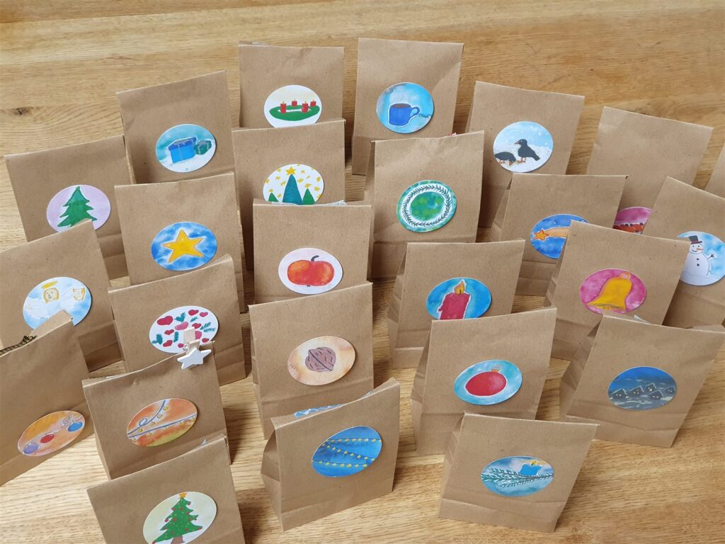 Braune Papiertüten mit bunten weihnachtlichen Bildsymbolen als selbstgemachter Rätsel-Adventskalender.