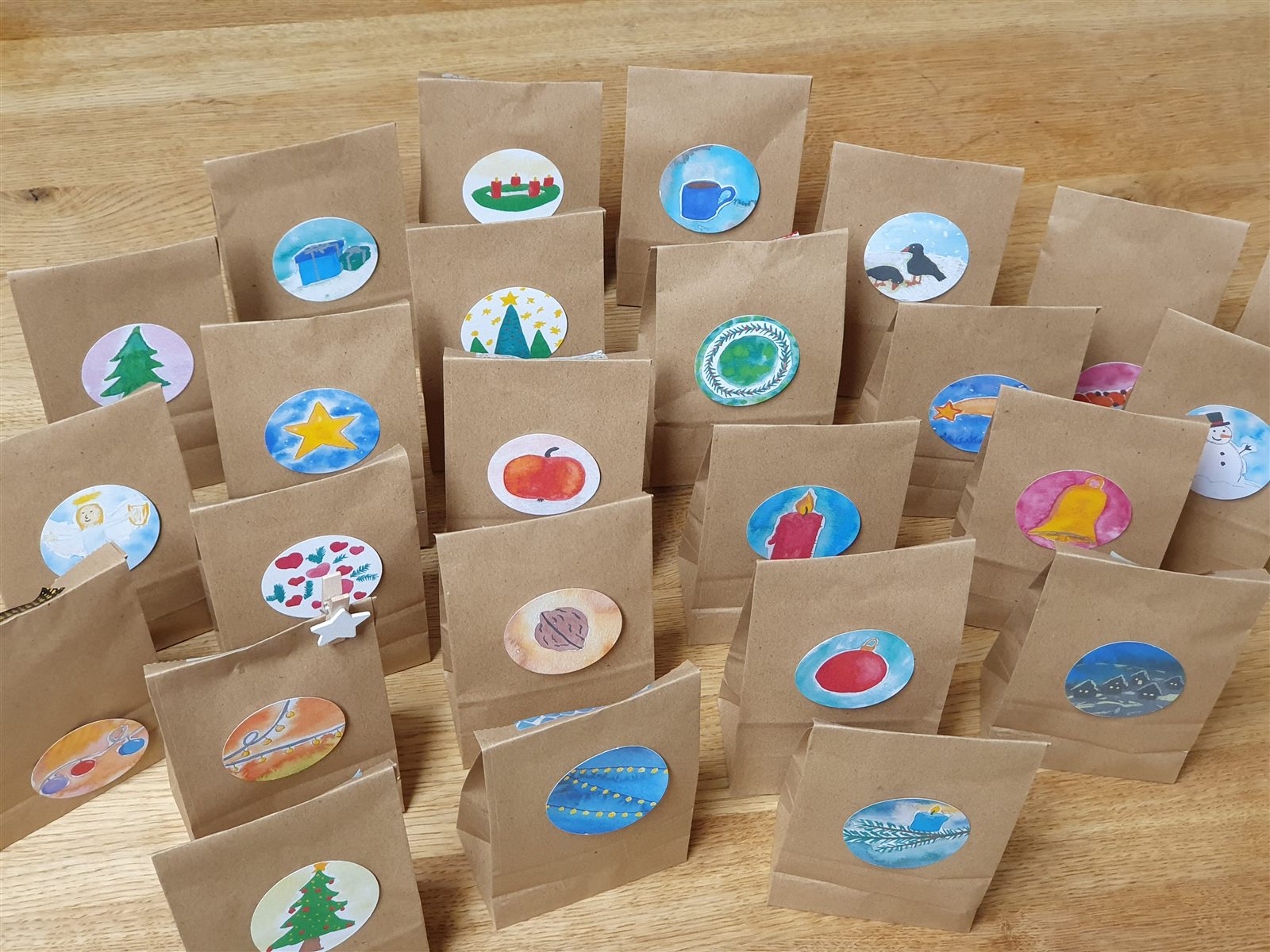 Braune Papiertüten mit bunten weihnachtlichen Bildsymbolen als selbstgemachter Rätsel-Adventskalender.